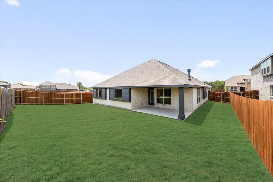 Rear view of brick home with covered patio, large grassy backyard, and wood privacy fence Rear view of brick home with covered patio, large grassy backyard, and wood privacy fence