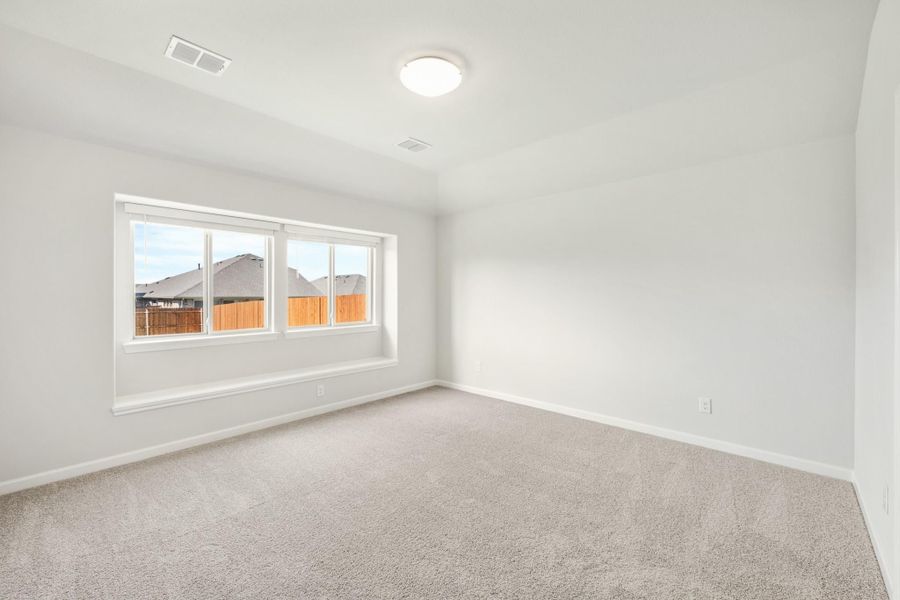 Empty bedroom with white walls, beige carpet, and a triple-pane window overlooking neighboring homes