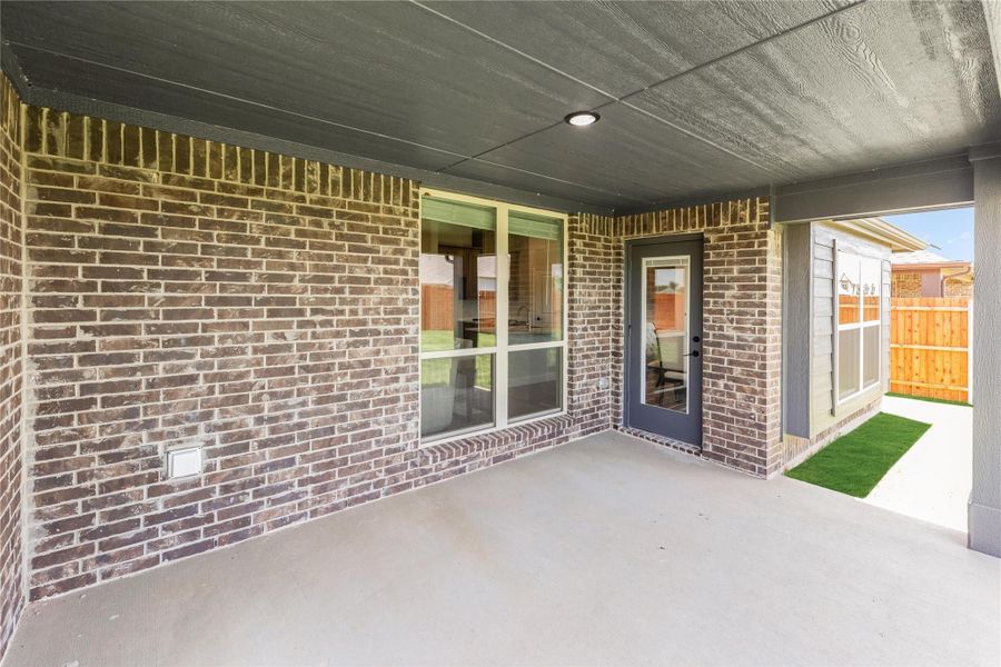 Covered back patio with brick exterior, sliding glass door, and entry door leading to fenced backyard