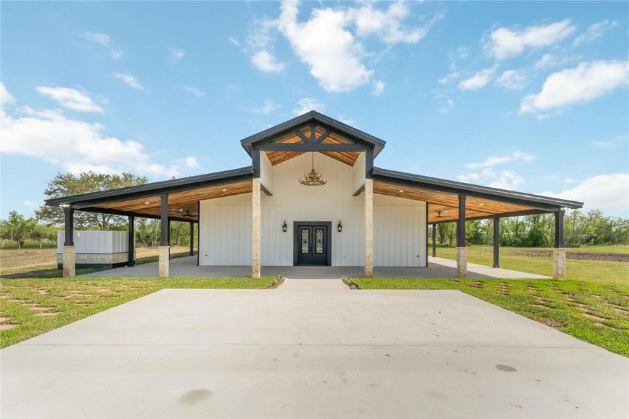 This photo showcases a modern farmhouse-style home with a spacious covered porch, high ceilings, and a sturdy metal roof, set on a large plot of land. Perfect for enjoying open-air living in a rural setting.
