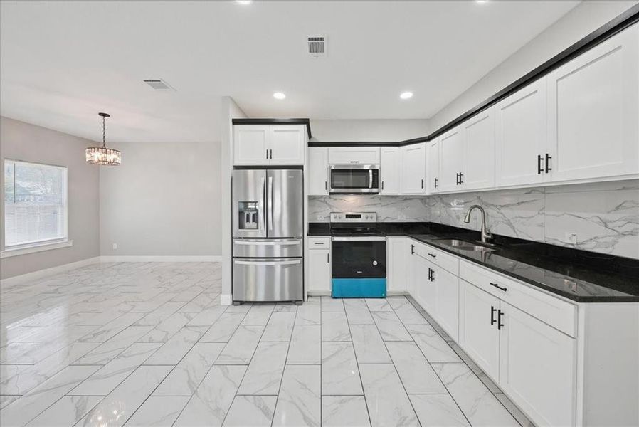 Kitchen featuring appliances with stainless steel finishes, decorative backsplash, white cabinets, light marble finish flooring, and recessed lighting
