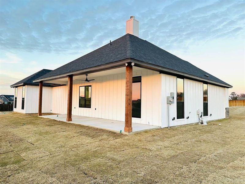 Back house at dusk featuring a lawn, ceiling fan, and a patio area