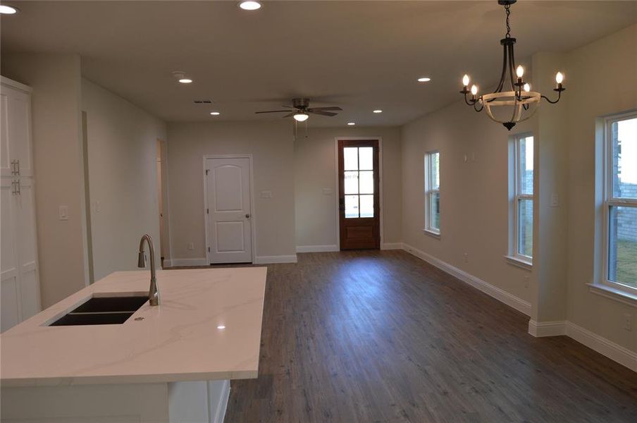 Kitchen with ceiling fan with notable chandelier, sink, decorative light fixtures, dark hardwood / wood-style floors, and an island with sink