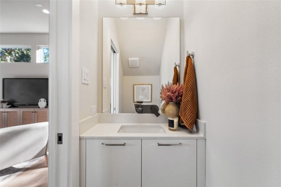 Elegant powder bath featuring a quartz countertop, sleek cabinetry & a large framed mirror that adds depth & sophistication to the space. Elegant powder bath featuring a quartz countertop, sleek cabinetry & a large framed mirror that adds depth & sophistication to the space.