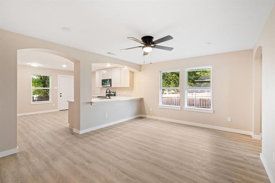 Unfurnished living room featuring arched walkways, ceiling fan, and light wood-style flooring