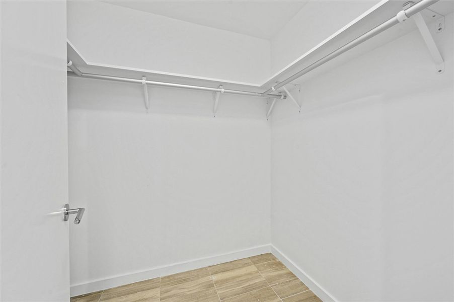 Generous walk-in closet with built-in shelving and double hanging rods, offering abundant storage and organization for a primary wardrobe. Generous walk-in closet with built-in shelving and double hanging rods, offering abundant storage and organization for a primary wardrobe.