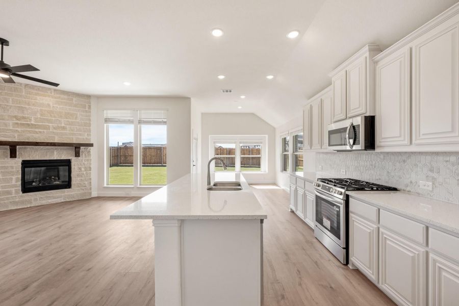 Open kitchen with white cabinets, large island, stainless appliances, and stone fireplace in adjoining living area Open kitchen with white cabinets, large island, stainless appliances, and stone fireplace in adjoining living area