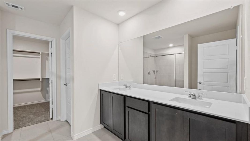 Bathroom vanity featuring dual sinks with chrome fixtures, a full-width mirror, and dark wood-finish cabinetry Bathroom vanity featuring dual sinks with chrome fixtures, a full-width mirror, and dark wood-finish cabinetry
