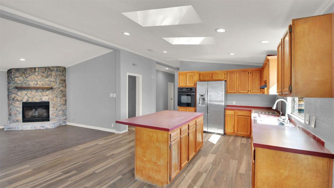 Kitchen with vaulted ceiling, open floor plan, stainless steel fridge with ice dispenser, a kitchen island, and light wood finished floors
