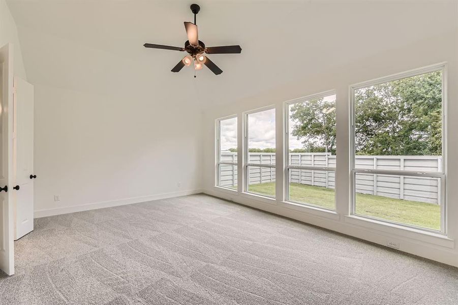 Carpeted empty room featuring healthy amount of natural light, a ceiling fan, baseboards, and high vaulted ceiling Carpeted empty room featuring healthy amount of natural light, a ceiling fan, baseboards, and high vaulted ceiling