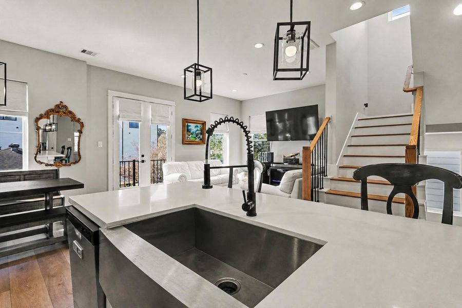 You will enjoy entertaining in the open-concept living space with a sleek kitchen island and stainless steel sink. The area is bright, featuring large windows, elegant pendant lighting, and an adjacent cozy living room with a staircase leading up.