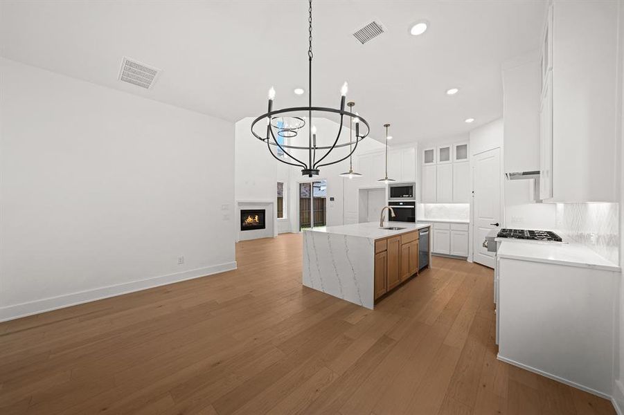 Kitchen with a chandelier, white cabinetry, open floor plan, light stone countertops, and light wood-style flooring