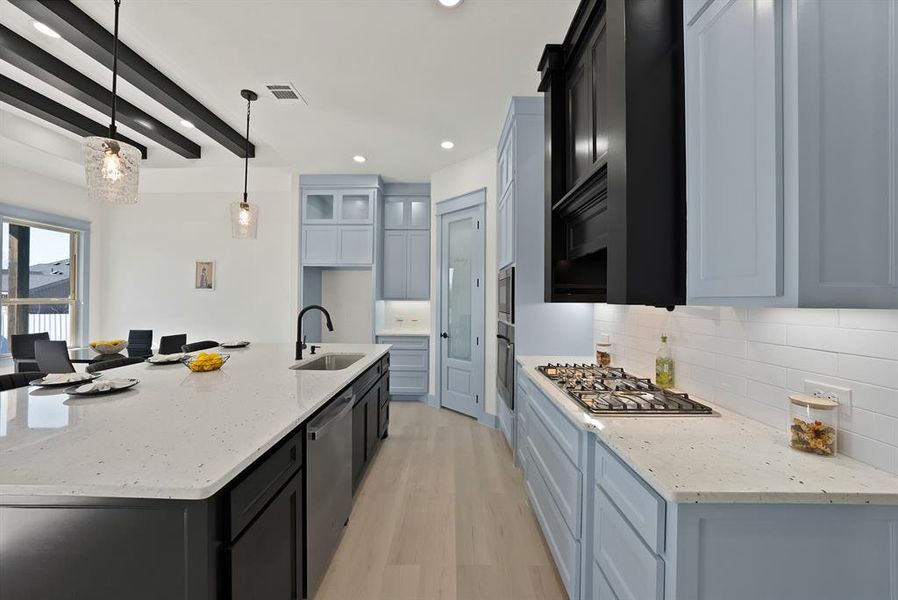 Kitchen with light stone counters, a large island, decorative light fixtures, light wood-style floors, and dark cabinets