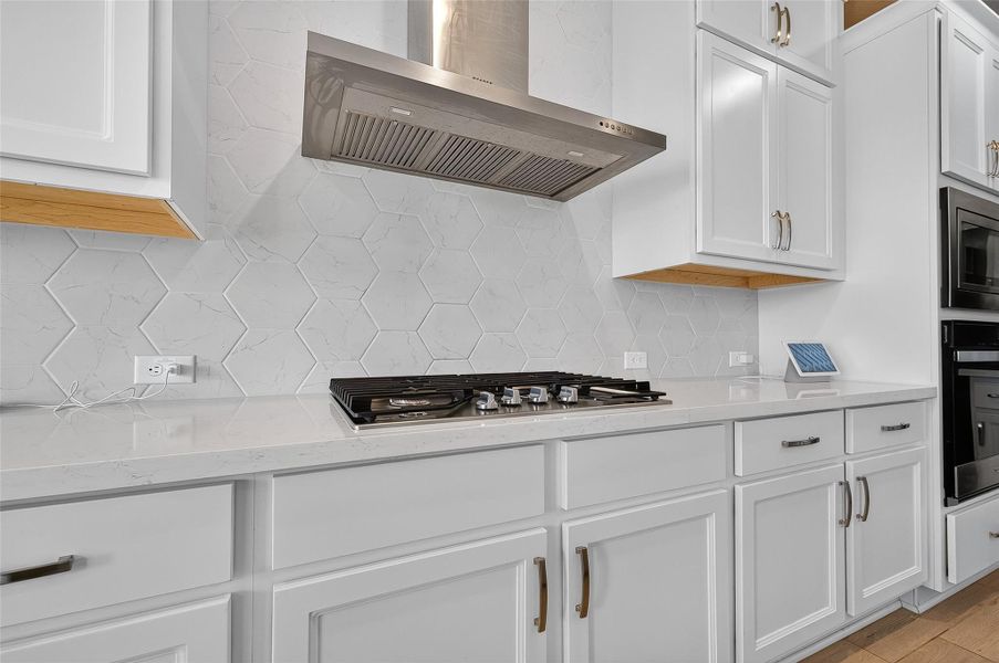 Sleek stainless steel vent hood and a 5-burner gas cooktop are framed by elegant quartz counters and abundant cabinet storage. The geometric tile backsplash adds a modern touch to this stylish culinary space.