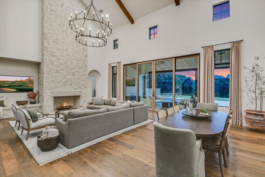 Dining space with a stone fireplace, a high ceiling, hardwood / wood-style floors, beamed ceiling, and a chandelier Dining space with a stone fireplace, a high ceiling, hardwood / wood-style floors, beamed ceiling, and a chandelier