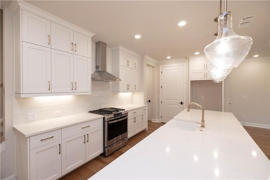 Kitchen featuring white cabinetry, stainless steel gas range, decorative backsplash, wall chimney range hood, and pendant lighting