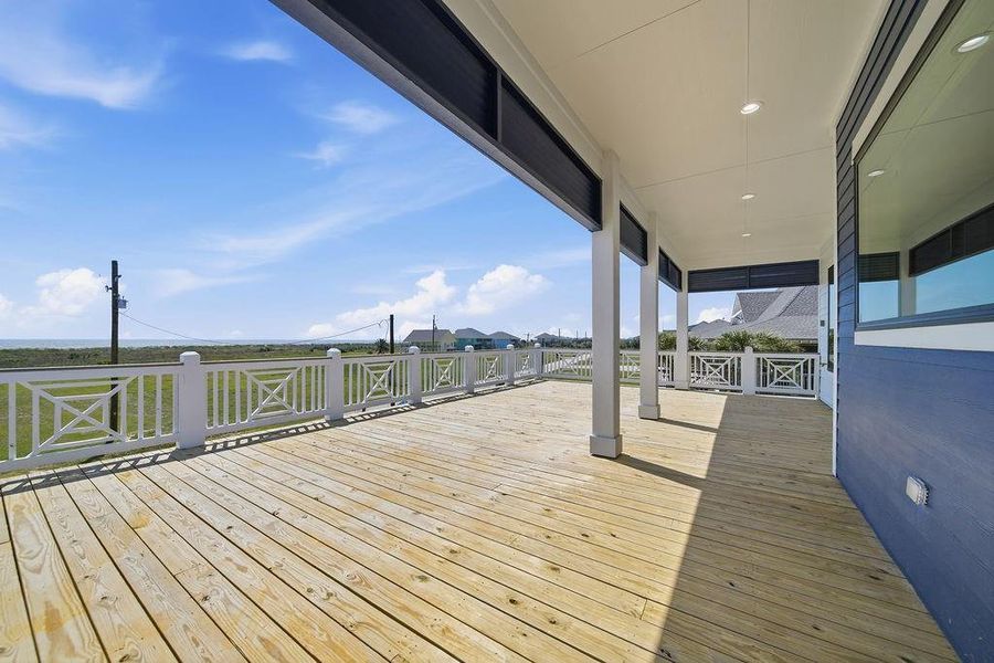 This photo showcases a spacious wooden deck with modern railings and partial covering, offering expansive views of open greenery and a bright blue sky—ideal for outdoor relaxation and entertaining.