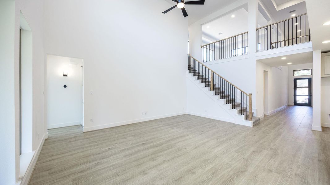Unfurnished living room with light wood finished floors, a towering ceiling, stairway, ceiling fan, and recessed lighting Unfurnished living room with light wood finished floors, a towering ceiling, stairway, ceiling fan, and recessed lighting