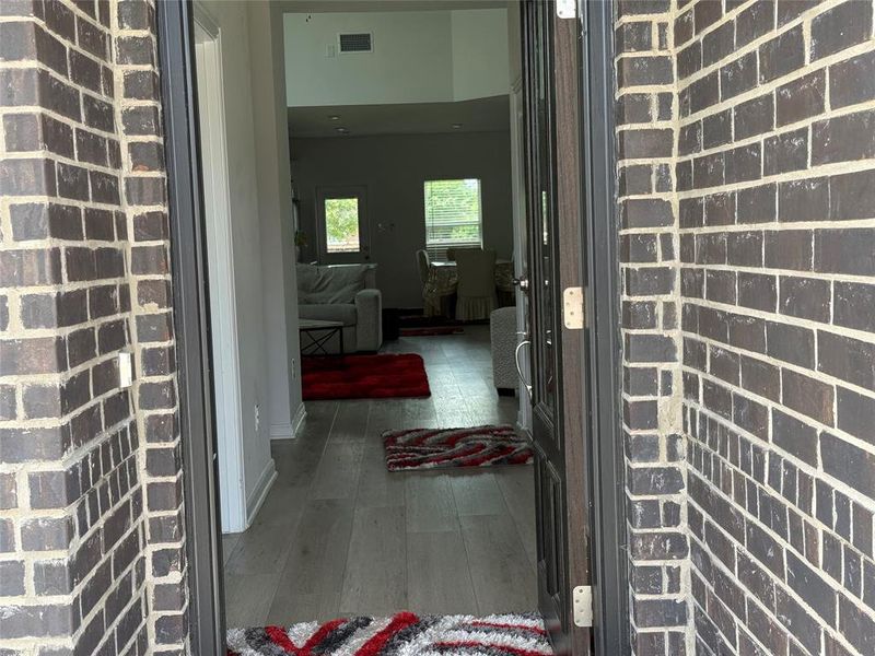 Entryway featuring dark brick exterior, a dark-framed entry door, light wood-finish flooring, and white baseboards
