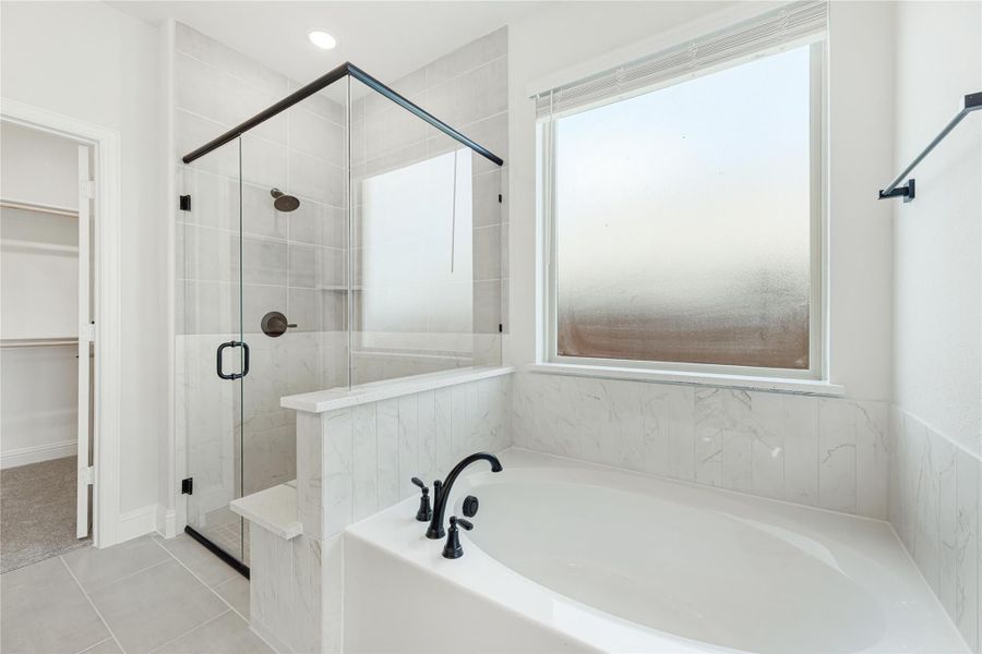 Master bathroom with soaking tub, glass-enclosed shower, marble tile walls, and black fixtures