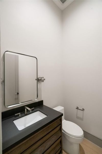 This photo shows a modern, compact bathroom with a minimalist design. It features a sleek vanity with a dark countertop, a rectangular mirror, and a standard toilet. The walls are light-colored, enhancing the room's brightness and simplicity.