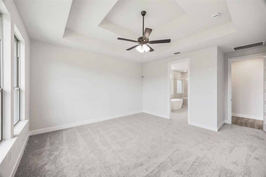Unfurnished bedroom with a raised ceiling, light carpet, a ceiling fan, and connected bathroom