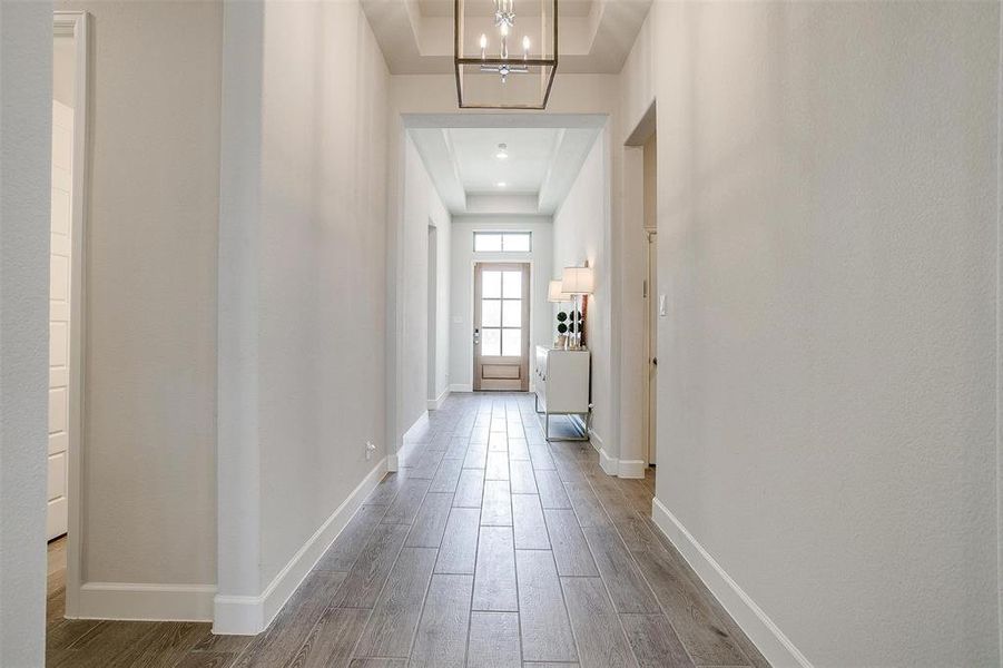 Hall featuring a tray ceiling, dark wood-style flooring, baseboards, and a chandelier Hall featuring a tray ceiling, dark wood-style flooring, baseboards, and a chandelier