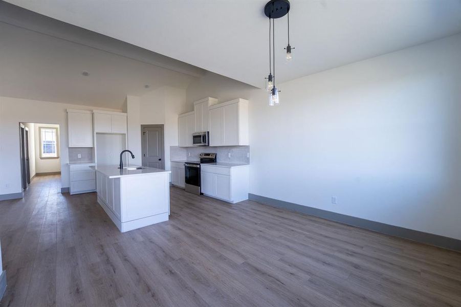 Kitchen with white cabinetry, a center island with sink, stainless steel appliances, and dark wood-style flooring Kitchen with white cabinetry, a center island with sink, stainless steel appliances, and dark wood-style flooring