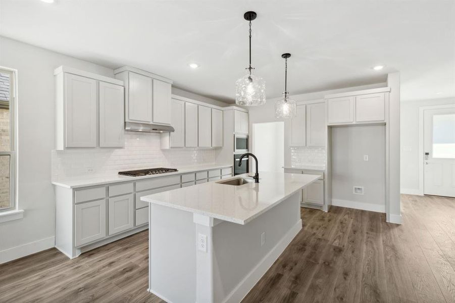 Kitchen with sink, a kitchen island with sink, dark hardwood / wood-style floors, pendant lighting, and appliances with stainless steel finishes