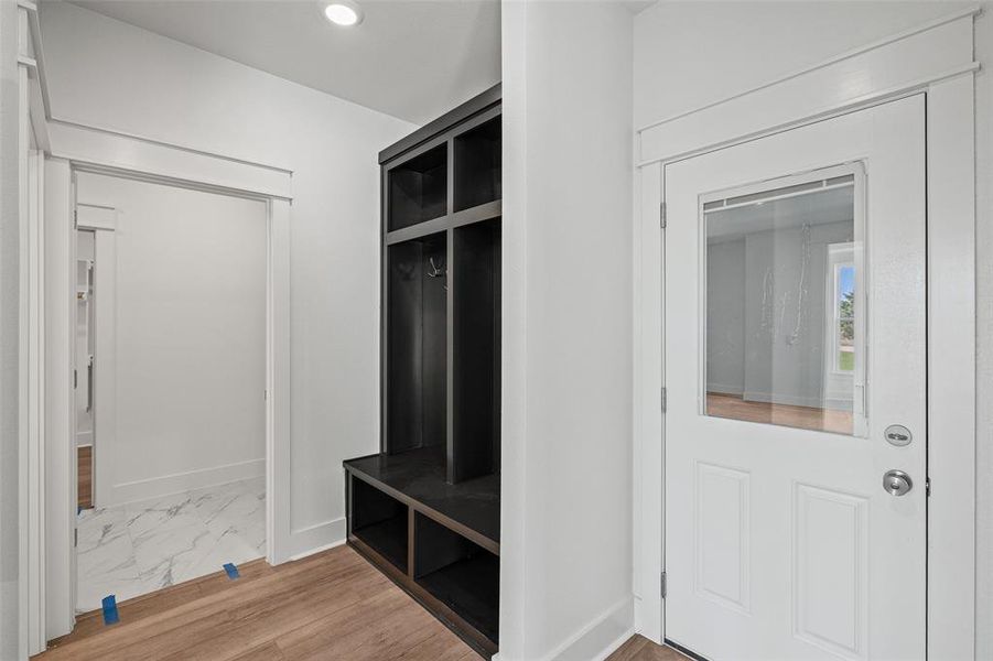 Entryway mudroom featuring built-in dark wood cabinetry with storage cubbies and coat hooks, wood-finish flooring, and a white paneled door with an integrated window