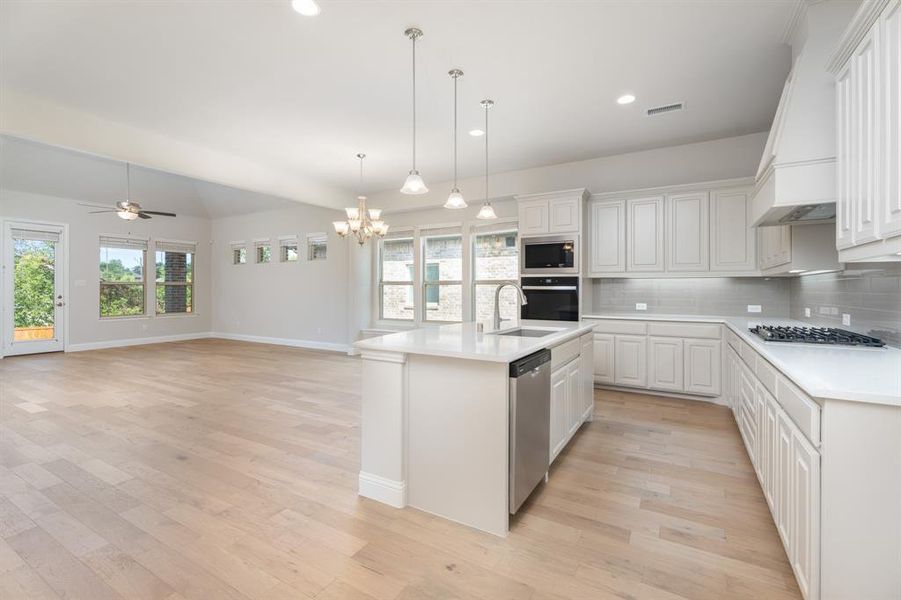 Kitchen with tasteful backsplash, decorative light fixtures, white cabinetry, light wood finished floors, and recessed lighting