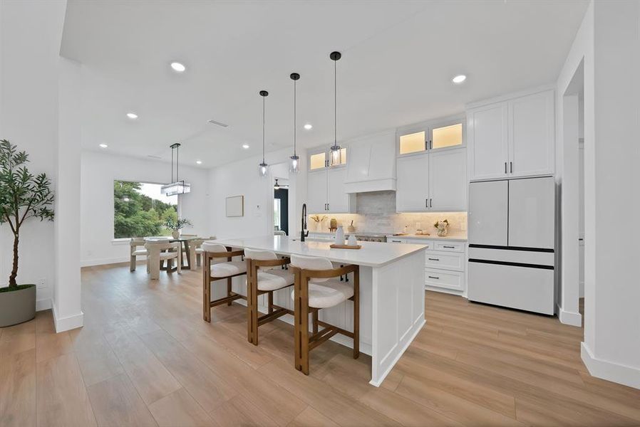 Spacious open-concept kitchen featuring a large central island with seating, white cabinetry, integrated appliances, recessed lighting, and wood-finish flooring