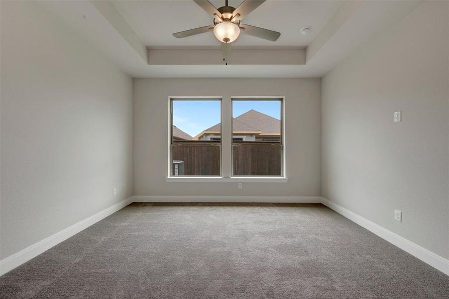 Spacious room featuring a tray ceiling, ceiling fan with integrated lighting, twin windows, neutral wall tones, and gray carpeting