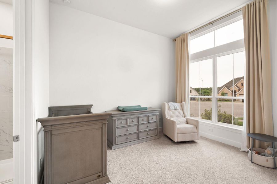 A well-lit bedroom features plush carpeting and a soaring window overlooking the neighborhood.