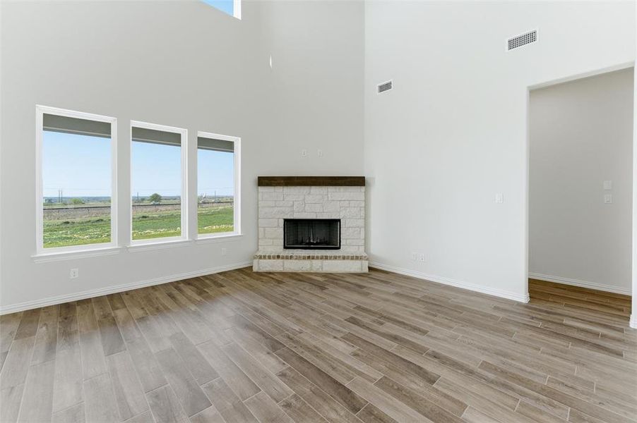 Unfurnished living room with a fireplace, wood finish floors, and a high ceiling Unfurnished living room with a fireplace, wood finish floors, and a high ceiling