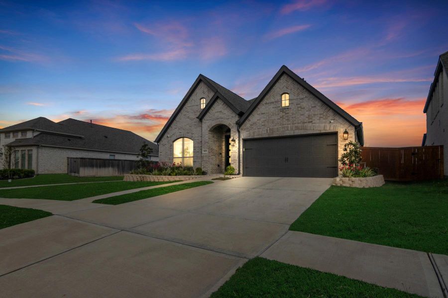 This charming brick home features a modern, single-story design with a spacious driveway leading to a double garage. The well-maintained lawn and landscaped garden beds add to its curb appeal. Perfectly situated at sunset, the warm exterior lighting highlights its inviting entrance.