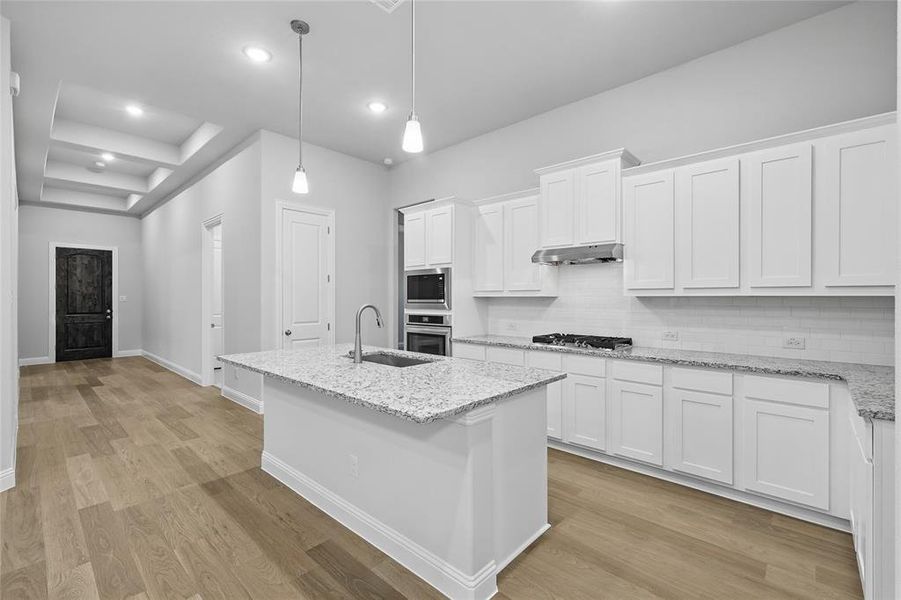 Kitchen featuring backsplash, white cabinetry, light wood-type flooring, light stone countertops, and recessed lighting Kitchen featuring backsplash, white cabinetry, light wood-type flooring, light stone countertops, and recessed lighting