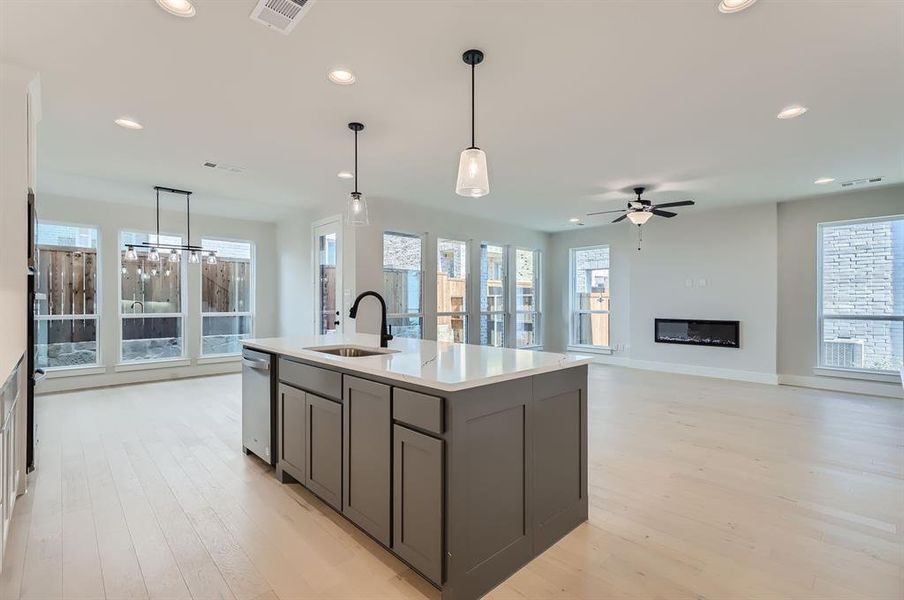 Kitchen featuring light hardwood / wood-style floors, a kitchen island with sink, sink, and pendant lighting