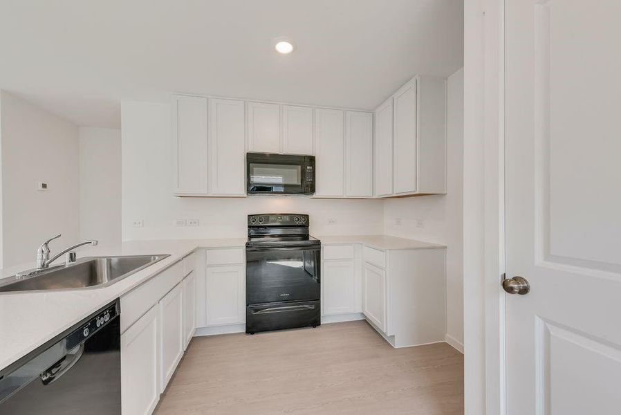 Kitchen with black appliances, light countertops, white cabinets, recessed lighting, and light wood-type flooring