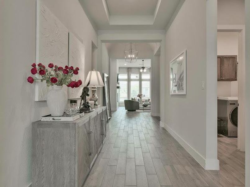 Corridor with wood tiled floors, washer / clothes dryer, a raised ceiling, and a chandelier Corridor with wood tiled floors, washer / clothes dryer, a raised ceiling, and a chandelier