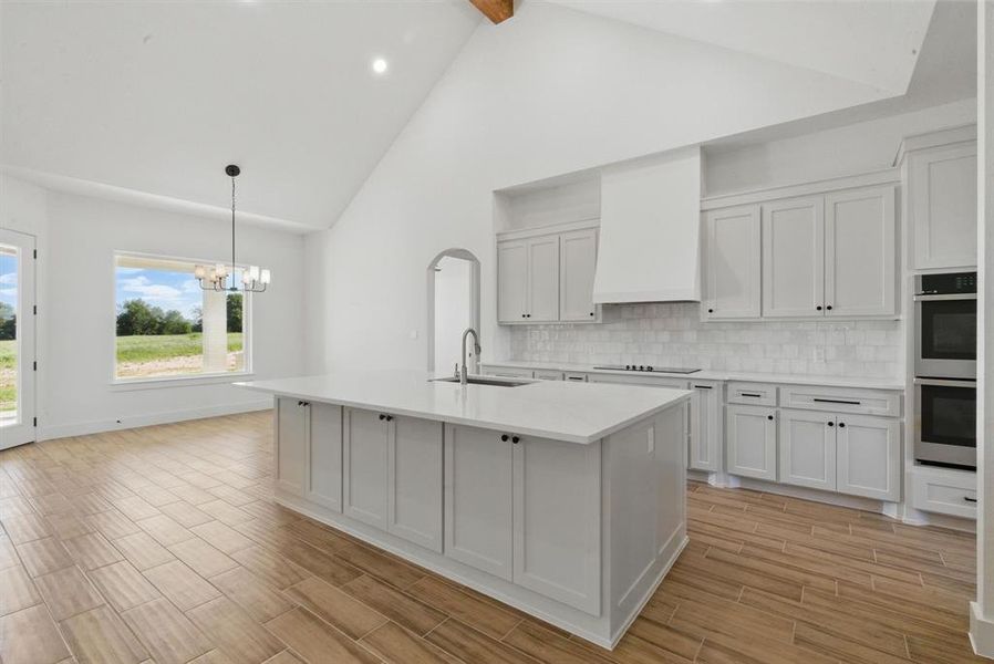 Kitchen featuring wood tiled floors, white cabinetry, backsplash, high vaulted ceiling, and pendant lighting Kitchen featuring wood tiled floors, white cabinetry, backsplash, high vaulted ceiling, and pendant lighting