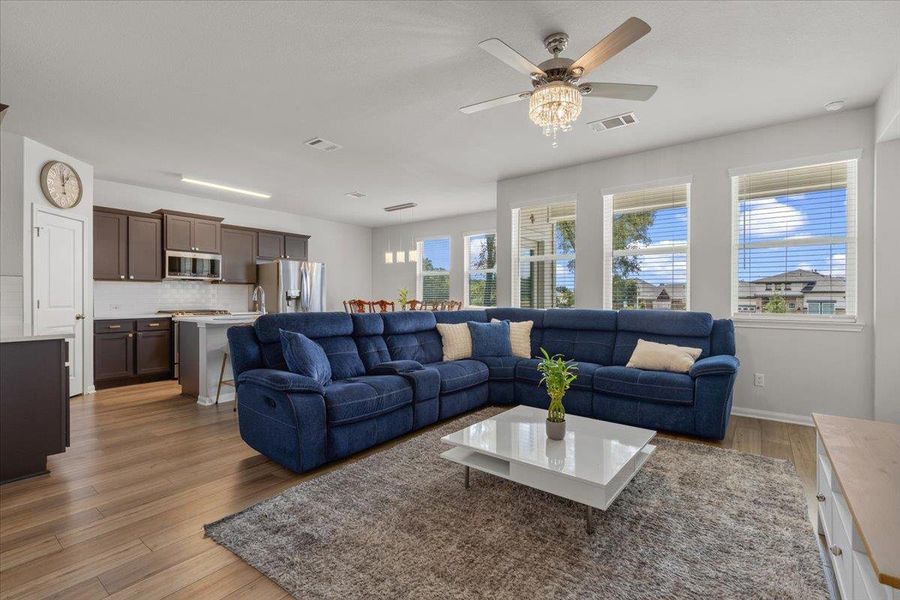 A spacious open-plan living room flows seamlessly into a modern kitchen with rich wood flooring.
