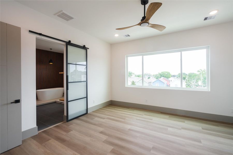 Representative Primary Bedroom View (Design selections and colors may vary): Located on the top level, the primary suite continues the refreshing style with clean lines, abundant natural light, and a touch of rustic charm featuring sleek glass barn doors to divide the closet and bathroom spaces.