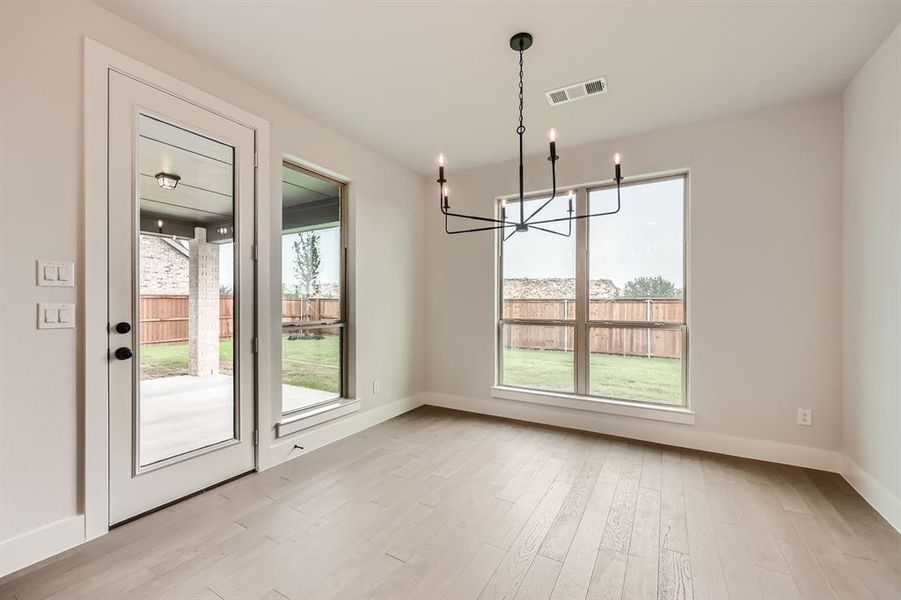 Unfurnished dining area featuring a wealth of natural light, visible vents, light wood-type flooring, and a chandelier Unfurnished dining area featuring a wealth of natural light, visible vents, light wood-type flooring, and a chandelier