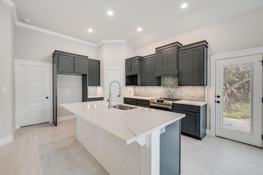 Kitchen with light stone countertops, a sink, stainless steel range with electric stovetop, decorative backsplash, and a center island with sink