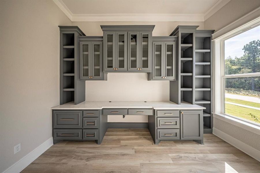 Unfurnished office featuring built in desk, crown molding, and light wood-style floors Unfurnished office featuring built in desk, crown molding, and light wood-style floors