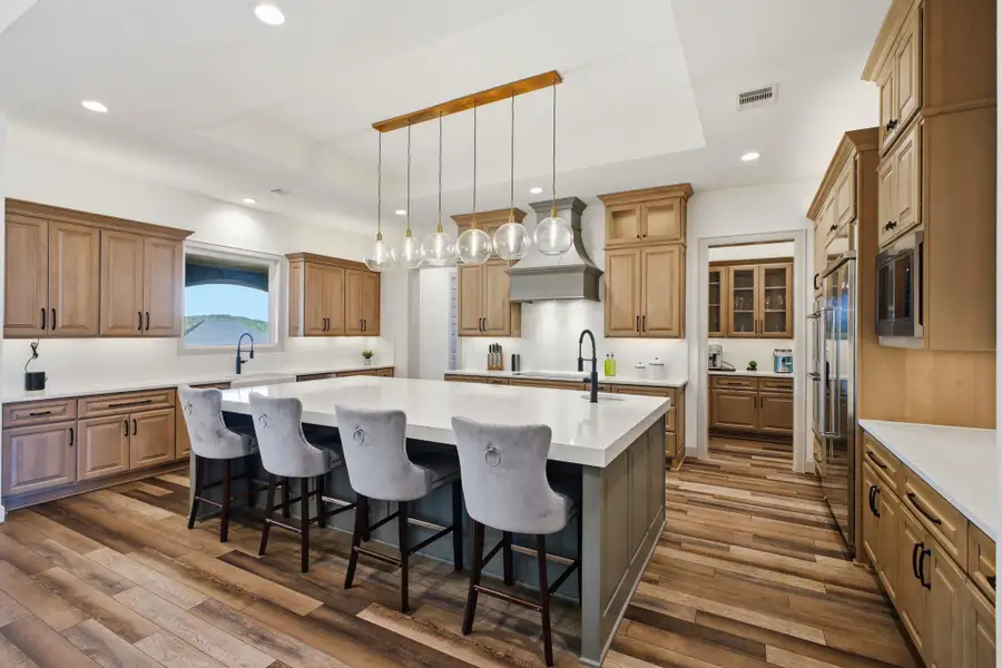The kitchen features a large island with seating, extensive cabinetry with black hardware, and wood-look flooring