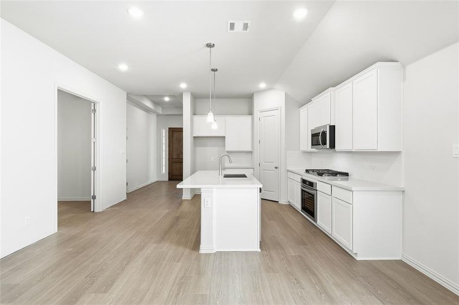 Kitchen featuring white cabinets, an island with sink, hanging light fixtures, light wood finished floors, and stainless steel appliances