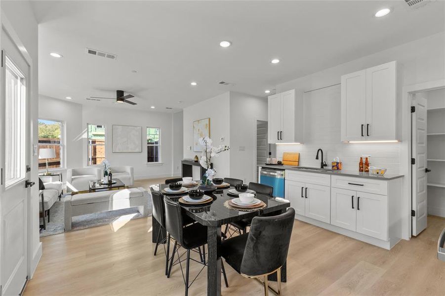 Open concept living space featuring light-toned flooring, recessed lighting, and a modern kitchen with white cabinetry, dark countertops, and a subway tile backsplash