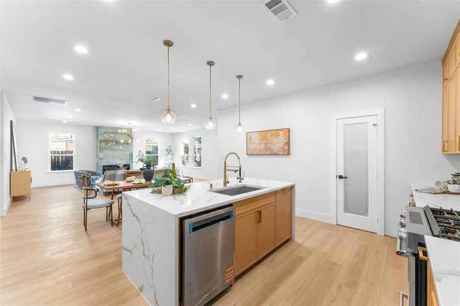 Kitchen featuring stainless steel appliances, open floor plan, light wood-style floors, light stone countertops, and light wood finish cabinetry